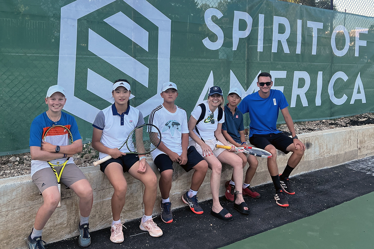 Serbian children sitting down at the tennis court in front of a Spirit of America logo